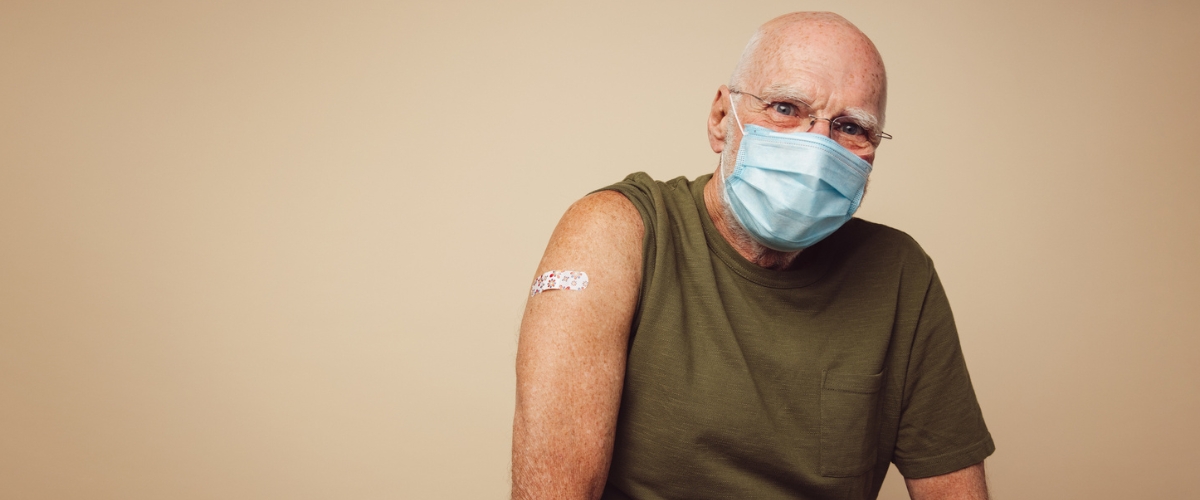 elderly man sitting in front of wall smiling with bandaid on arm from getting his flu shot.