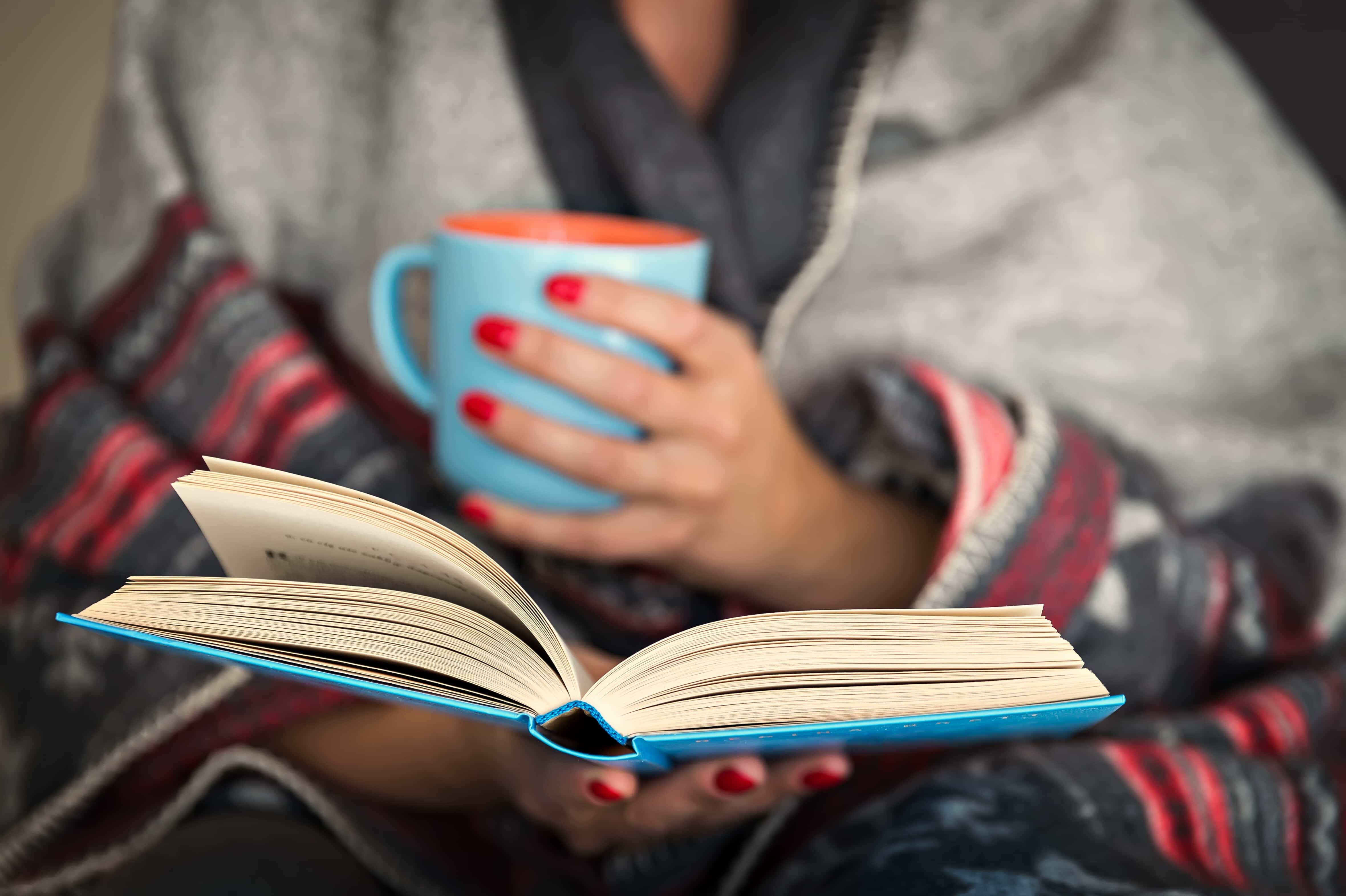 Woman reading a book with a mug of tea
