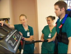 Jordan Olean (Physical Therapist) tests out the harness while Rachel Warpeha (Physical Therapist) and Nicole Koecher (Physical Therapist Assistant) examine the treadmill settings